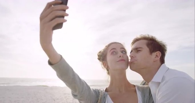 Happy couple taking selfies using mobile phone on beach at sunset