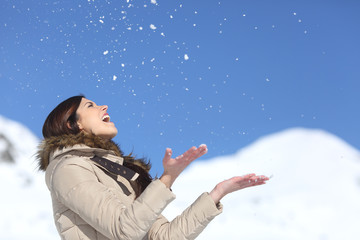 Happy woman throwing snow in the air on winter holdays