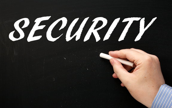 Hand writing the word Security in white text on a blackboard using a chalk stick