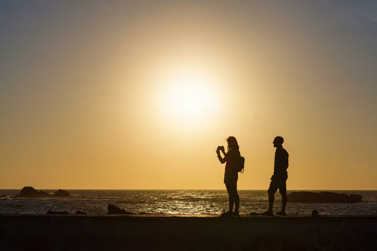 Silhouette of couple taking pictures by the sea