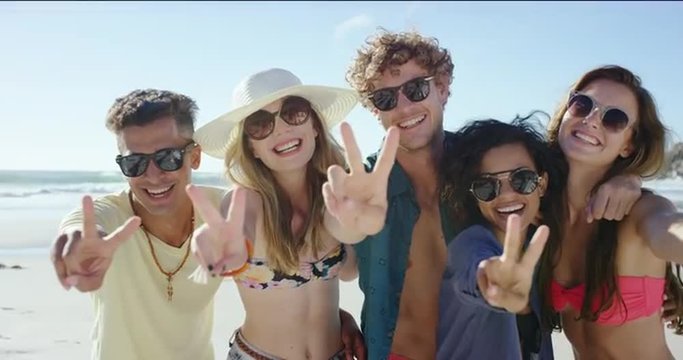 Group of friends smiling and making peace sign at camera for a portrait on the beach