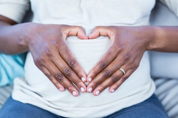 Mid section of woman making heart shape on her belly