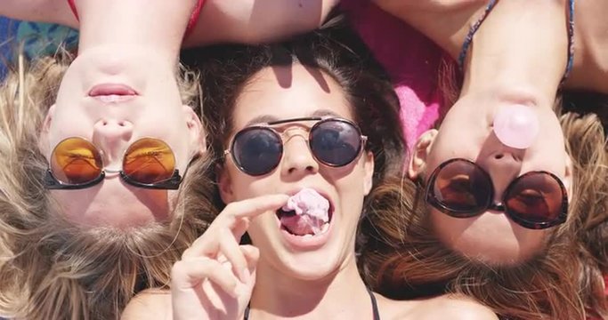 Top view of three teeanage girl friends lying on back blowing bubblegum candy bubbles on beach