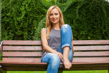 Obraz premium Sensual blonde woman sitting in park on wooden bench. Outdoor ph