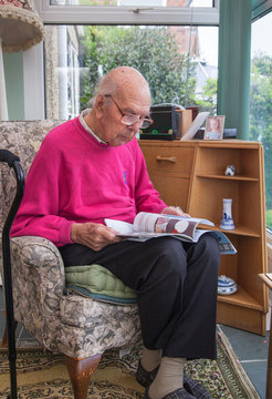 95 years old English man in domestic interior, reading local life magazine. Health, care and medicine concept