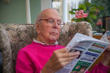95 years old English man in domestic interior, reading local life magazine. Health, care and...