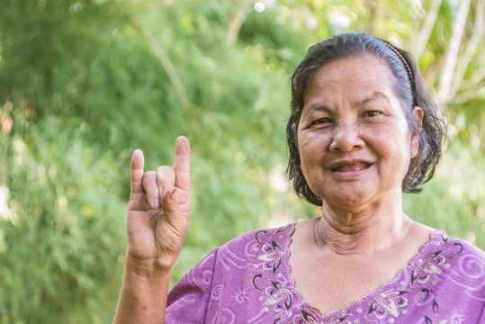 Old Thai woman smiling and willing to show I love you hand sign