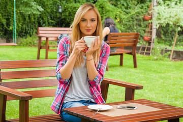 Portrait of young beautiful woman sitting in a garden outdoor drinking coffee.