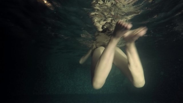 Underwater view of swimming girl in dark pool side view. UHD 4K stock footage