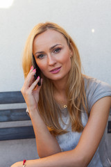 Fototapeta premium Sensual blonde woman sitting on wooden bench. She is using mobile phone.