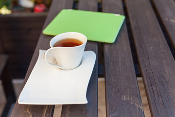 Tablet pc in green cover and cup of tea on wooden table. Relax concept.