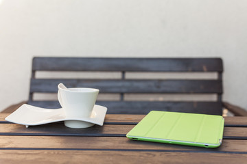 Tablet pc in green cover and cup of tea on wooden table. Relax concept.