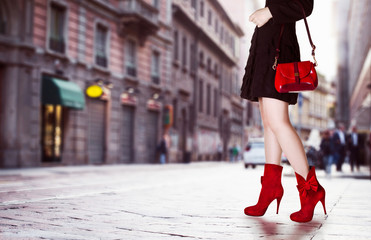 A girl with red bag and red boots in the street. Black coat.Beautiful legs in autumn winter time. 