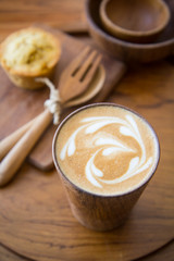 Latte art coffee on wooden cup with pumpkin muffin