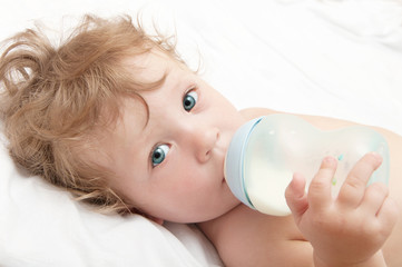  little curly-headed baby sucks a bottle of milk