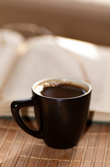 cup of coffee, standing next to an open book, on which lie glass