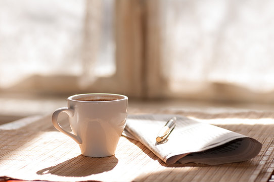 Fototapeta Cup of black coffee, newspaper and a pen against the window in t