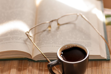 cup of coffee, standing next to an open book, on which lie glass
