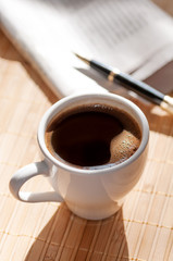 Cup of black coffee, newspaper and a pen