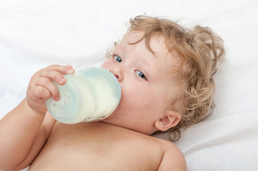 little curly-headed baby sucks a bottle of milk