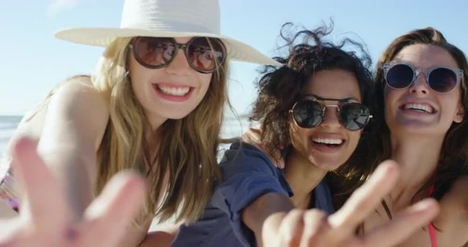 Three girl friends making peace sign smiling for photograph on the beach on summer vacation