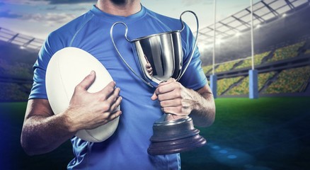 Composite image of rugby player holding trophy and ball
