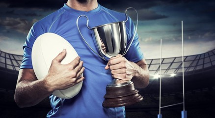 Composite image of rugby player holding trophy and ball