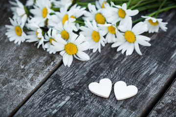 Fototapeta na wymiar Beautiful fresh daisies decorated with hearts on wooden texture