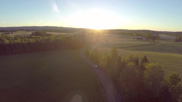 Flying over crops and cars on country road in sunset
