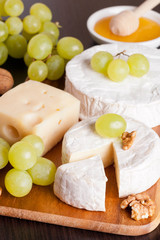 cheeses, honey, grapes and walnuts on a wooden background