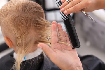 Fototapeta premium Skilled young female hairdresser is making haircut for kid