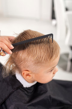 Professional young beautician is making hairstyle for child