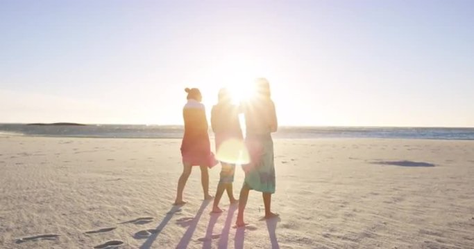 Three girl friends wrapped in towels keeping warm on windy beach 