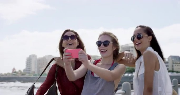 Three teenage girls taking selfie using smartphone on vacation outdoors beach promenade