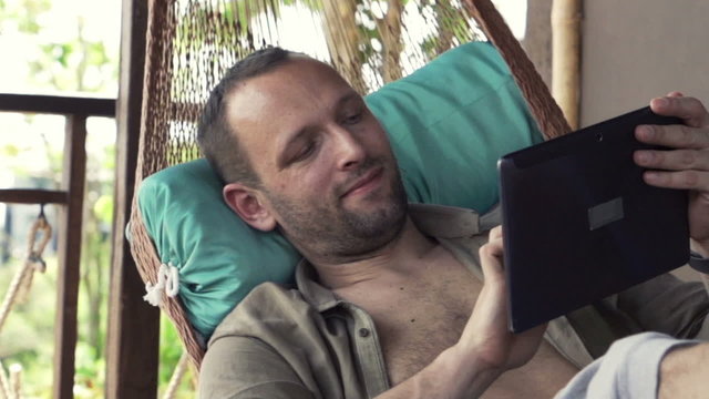Young man using tablet computer while lying on hammock, slow motion 240fps
