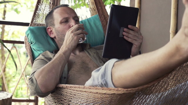 Man reading news on tablet computer and drink water on hammock, slow motion 240fps
