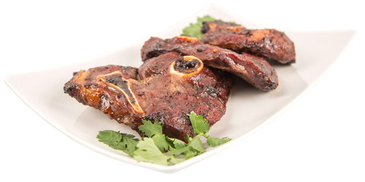 Roasted pieces of lamb on white plate over white background