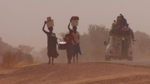 Women walk carrying goods on their heads through the Sahara desert in Mali.