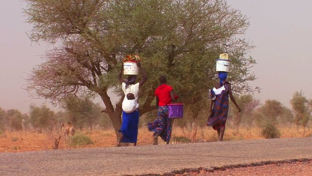 Women walk carrying goods on their heads through the Sahara desert in Mali.