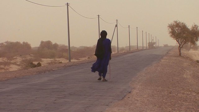 A Touareg person walks down a road through the Sahara desert in Mali.