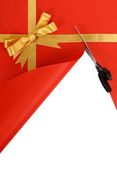 Gold gift bow and ribbon for christmas or birthday present being cut open with scissors unwrapping opening red wrapping paper background photo vertical