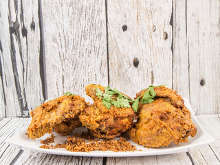 Popular Javanese dish Ayam Penyet or crispy fried chicken in a white plate over wooden background