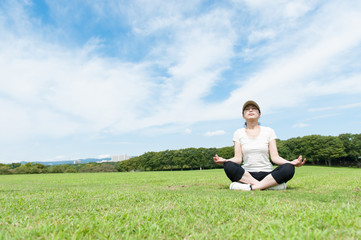Naklejka na ściany i meble 芝生の上に座って瞑想している女性