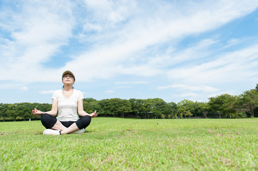 Naklejka na ściany i meble 芝生の上に座って瞑想している女性