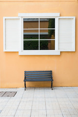 sidewalk scene with wooden bench and orange wall and window