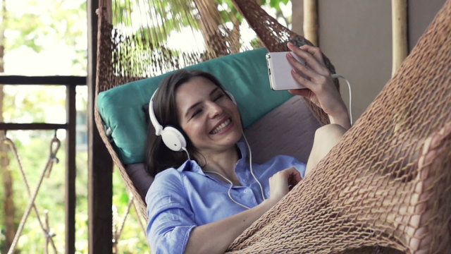 Happy woman watching movie one smartphone lying on hammock
