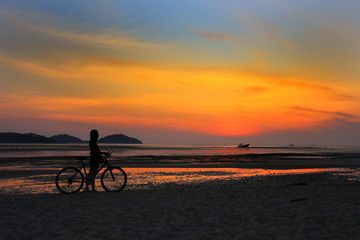 Fototapeta premium Silhouette of lonely unidentified girl with bike on beach with sunset light