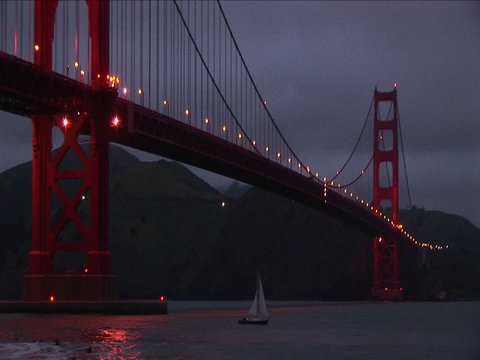 A worms-eye view of the Golden Gate Bridge at night with its lights reflecting on the water.