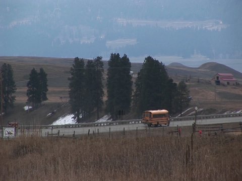 A yellow school bus travels along a rural road to pick up its passengers.