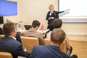 Photo of successful businesswoman reading lecture to his colleagues at presentation of new project and pointing on the white screen